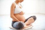 Waiting for a baby. Close-up of pregnant woman touching her belly while sitting in lotus position