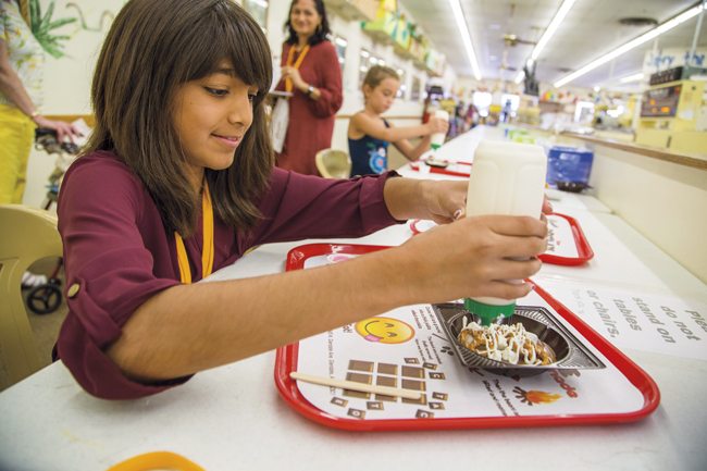 Nandini Patel (10), makes a chocolate pizza at Cerreta Candy Co. Her mom, writer Rudri Bhatt Patel, watches from behind. Also pictured: Presli Turner (8) of Peoria. . Photo by Tac Coluccio.
