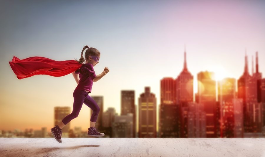 Little child girl plays superhero. Child on the background of sunset sky. Girl power concept