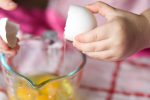 Child cracking eggs in the kitchen
