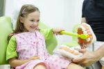 Girl in dentists chair toothbrushing a model