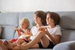 Cute children, sitting on couch, eating pizza and watching TV. Hungry child taking a bite from pizza on a pizza party