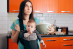 Busy Mom Cooking  Holding Baby in Carrier Babywearing System