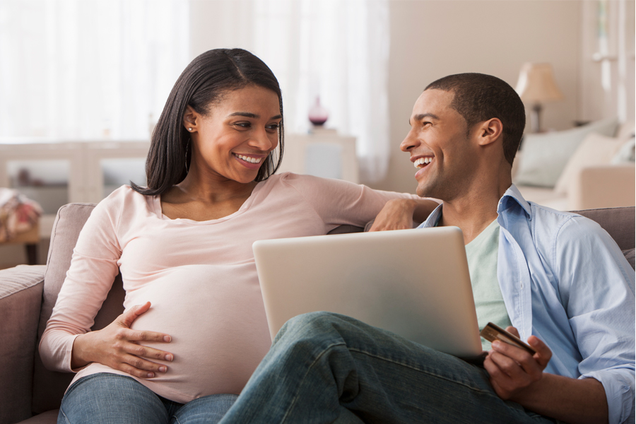 Pregnant woman and her partner sit on a couch doing research for hospital bags.